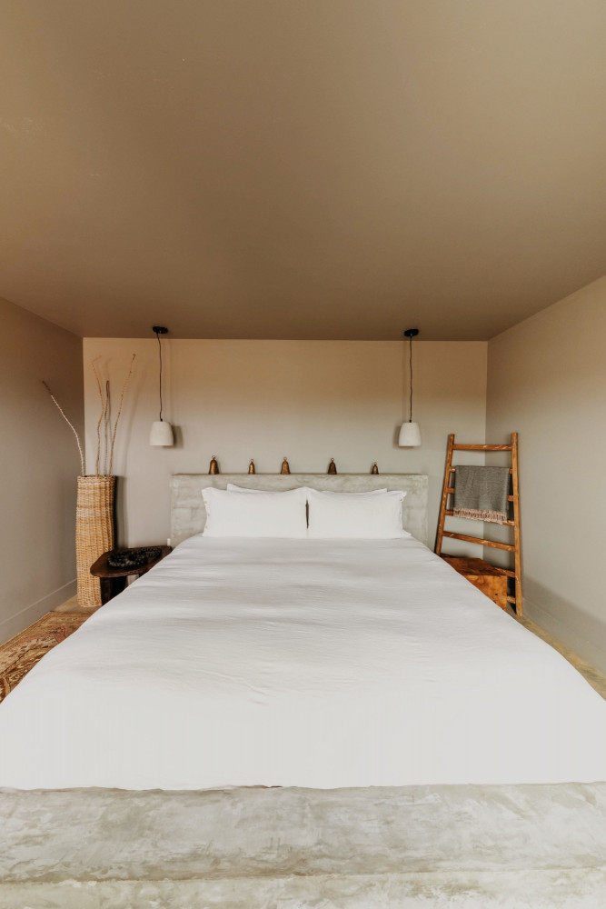A wide view of a minimalist guest room with a large bed, wooden ladder, and pendant lights.