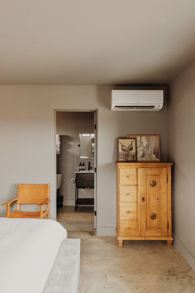 A wide view of a guest room with a bed, chair, wooden cabinet, and open doorway to bathroom
