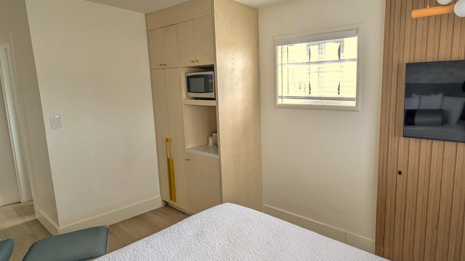A hotel room with a bed, TV, microwave, and cabinet.