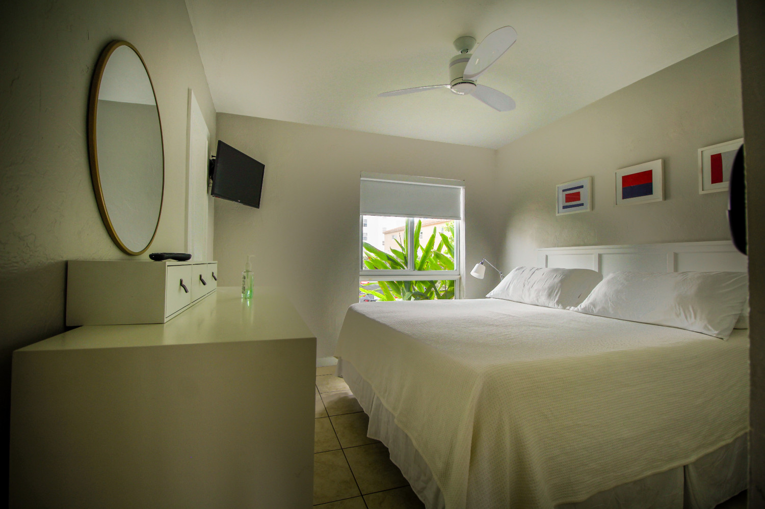 A hotel room with a large bed, window, dresser, and mirror