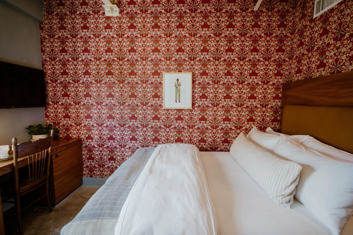 A hotel room with a large bed, wooden furniture, and red and white floral wallpaper.