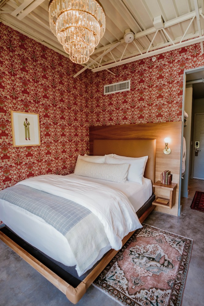 A hotel room with a large bed, red floral wallpaper, and a chandelier.