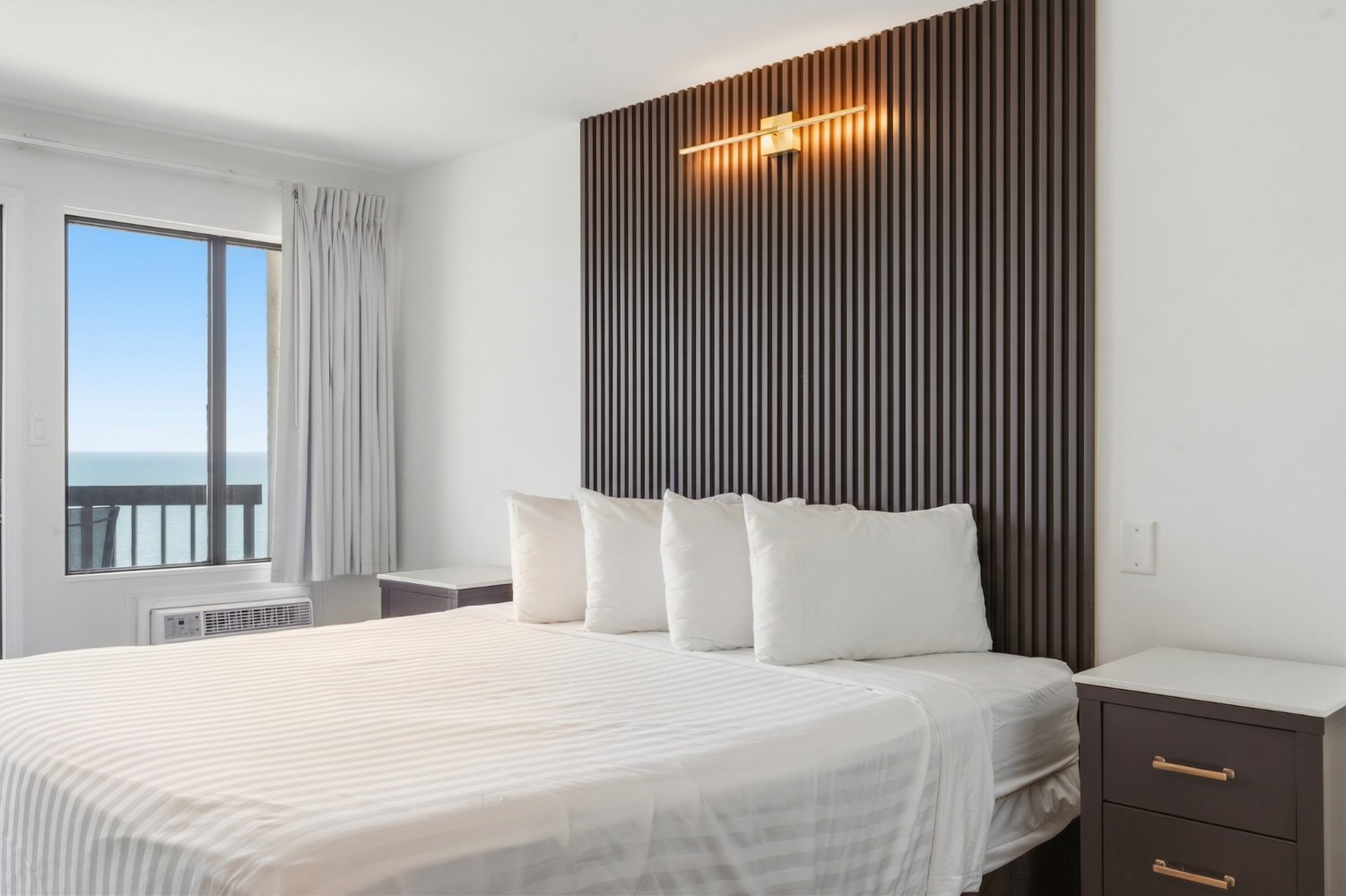 A hotel room with a large bed, nightstand, and window with an ocean view.