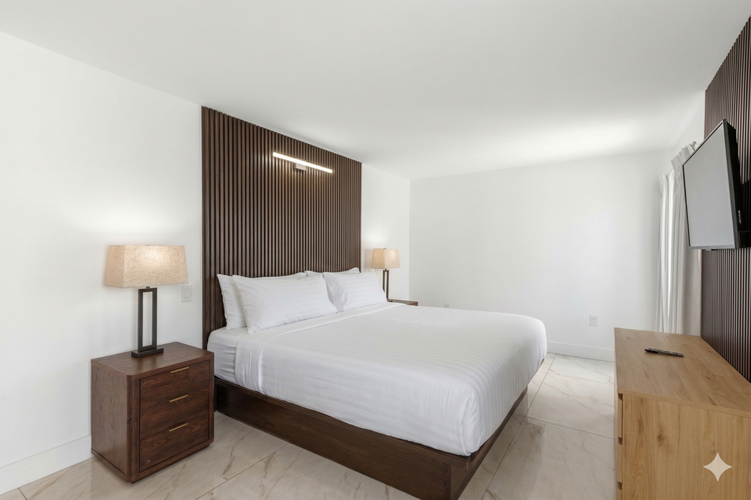 A clean and modern hotel room with a queen-sized bed, wooden accents, and a flat-screen TV.