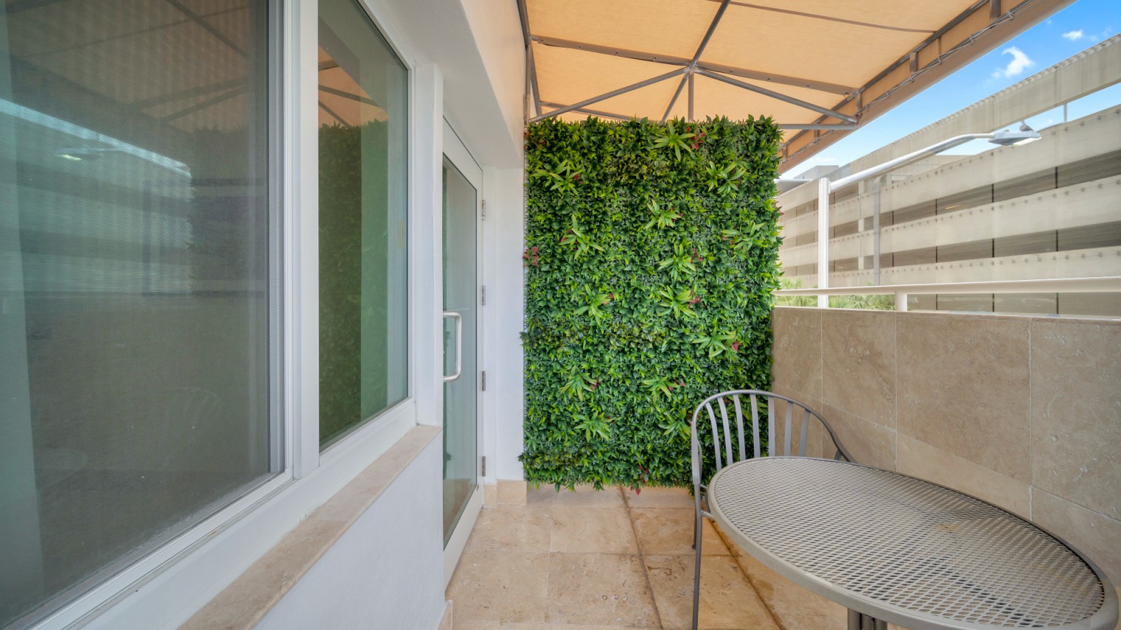 A small balcony with a green wall, a metal chair and table, and a beige umbrella.
