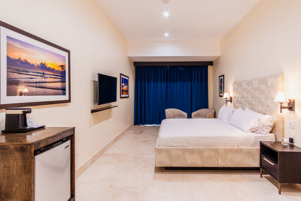 A hotel room with a king-sized bed, flat-screen TV, mini fridge, and coffee maker.