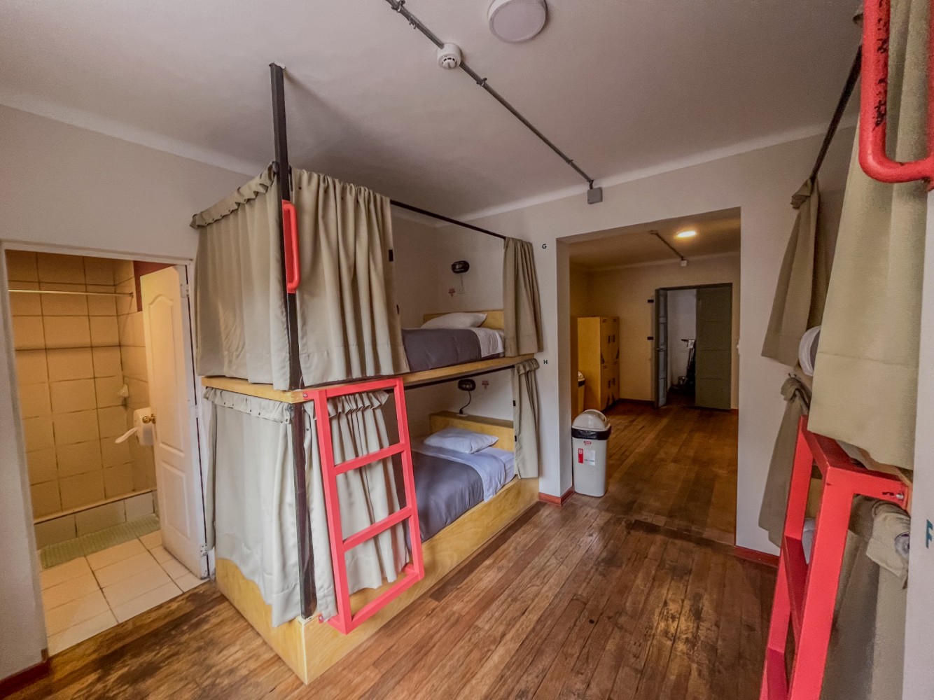 A wide view of a room with bunk beds, a bathroom in the background, and an open doorway.