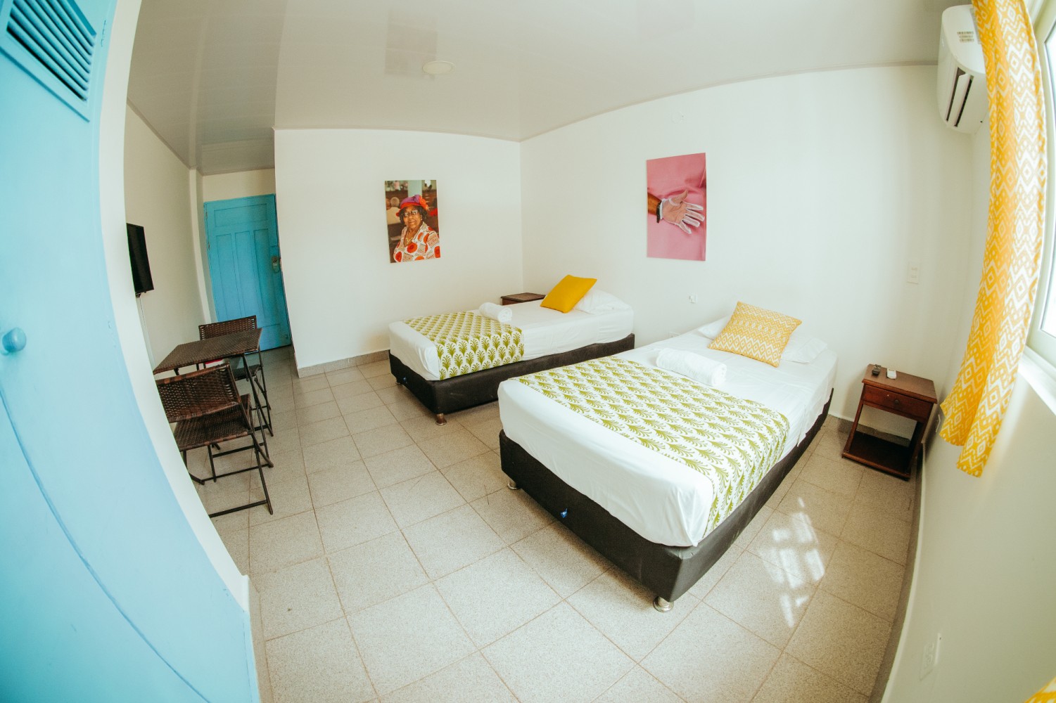 A wide-angle view of a hotel room with two beds, a desk, and artwork on the walls.